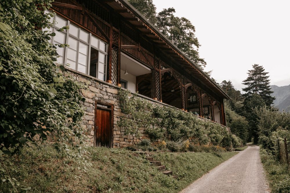 Rustic stone and wood building covered in ivy along a quiet countryside road in the mountains.