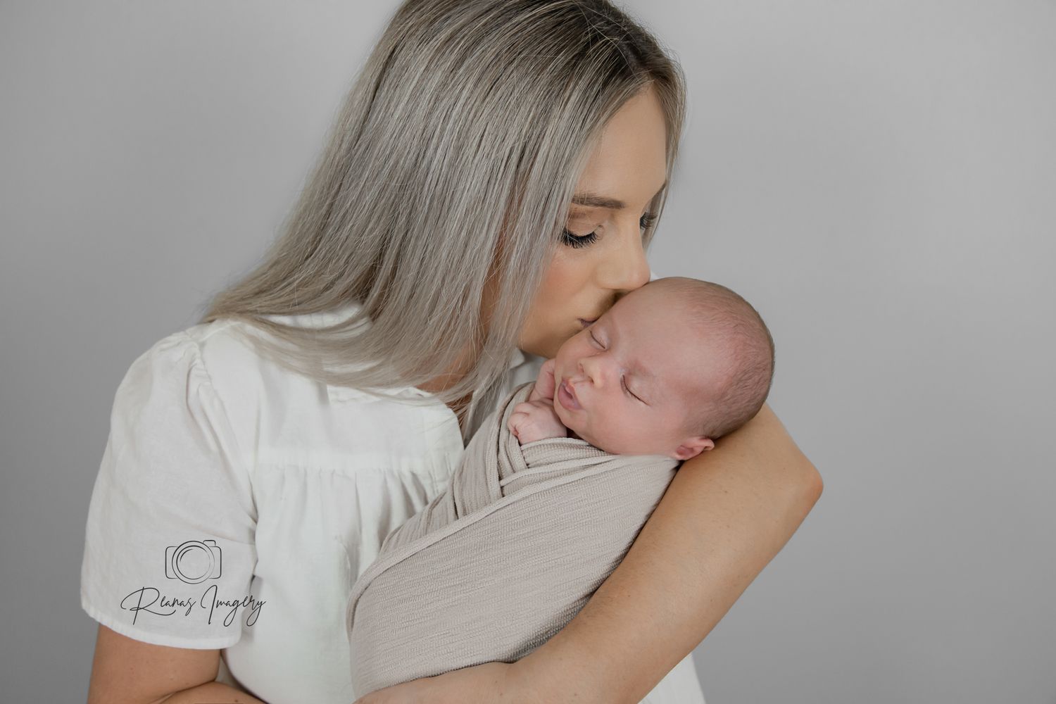 Woman with silver hair gently kissing sleeping newborn baby in studio portrait.
