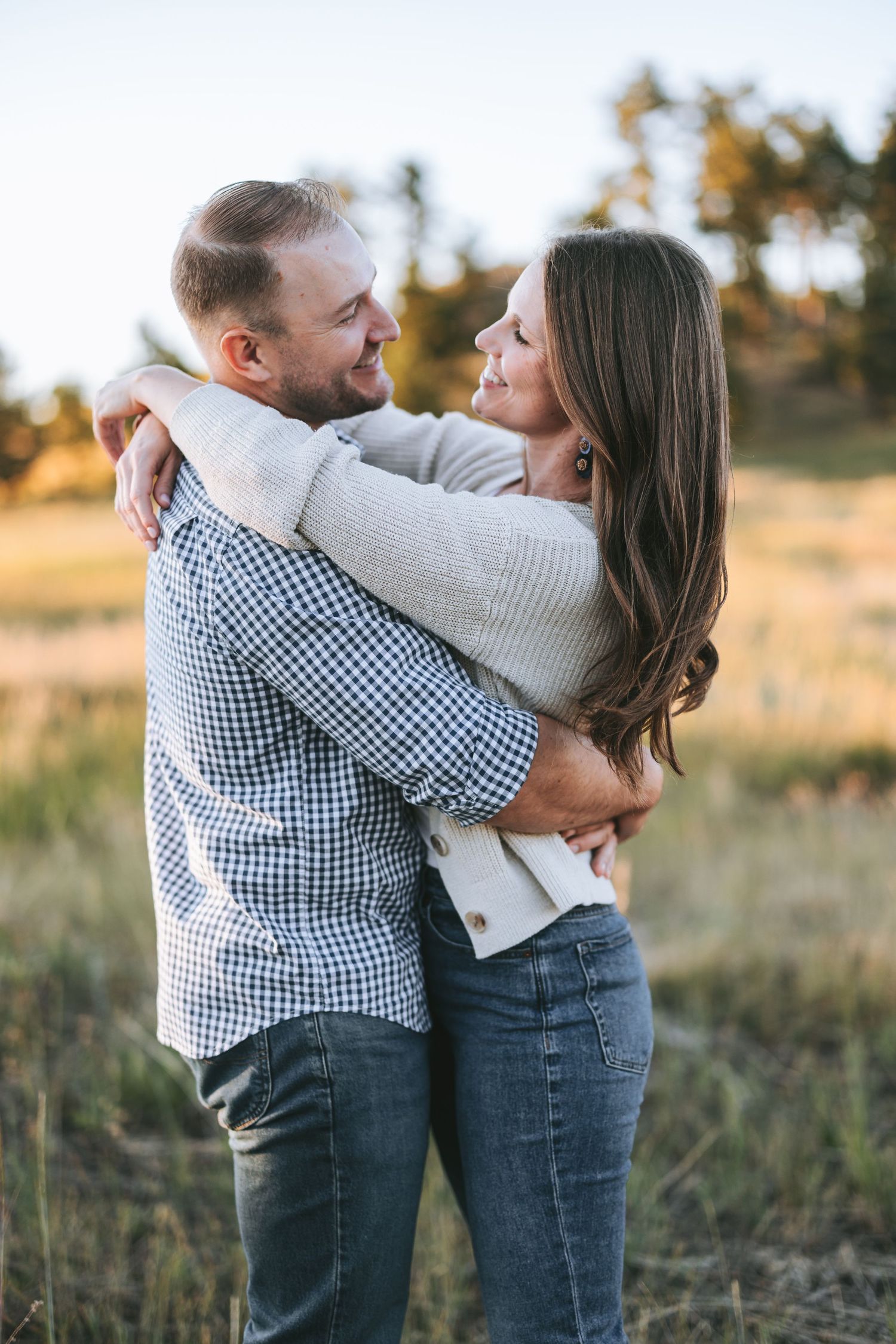 A couple in casual attire embraces while laughing in a sunlit meadow.