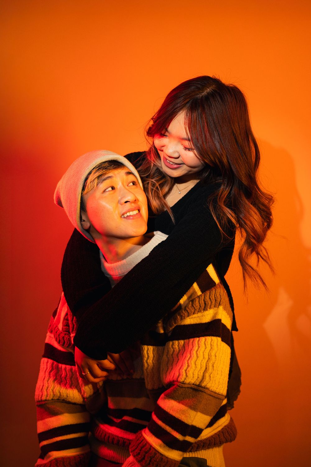 Candid portraits against vibrant orange background showing playful interaction.