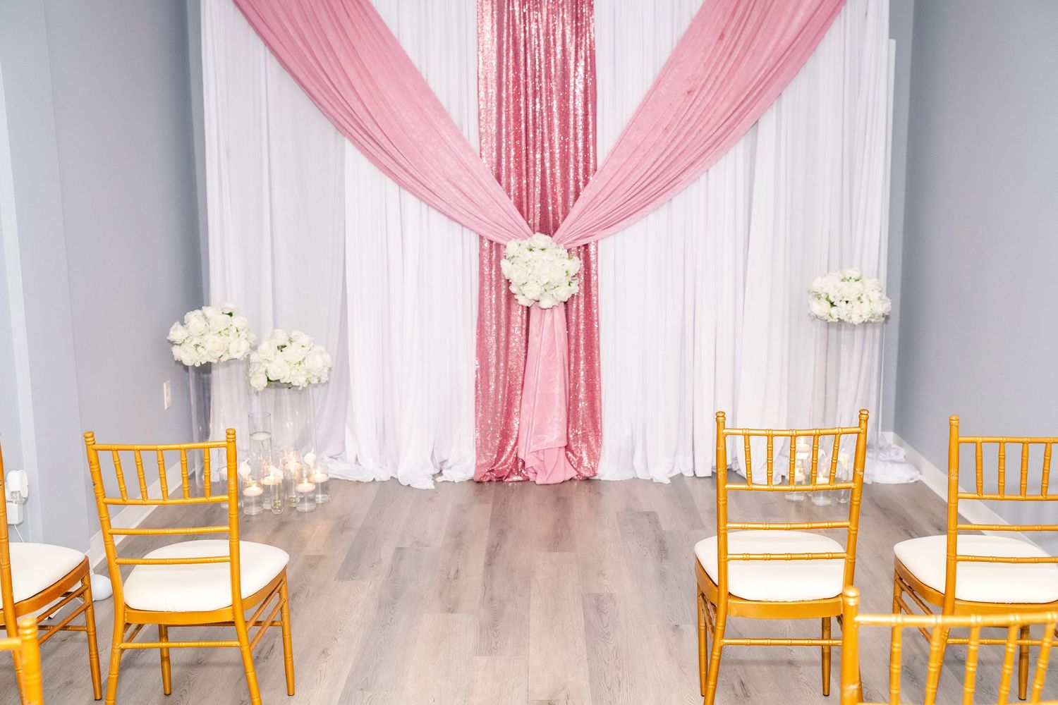Gold chiavari chairs arranged neatly in front of white draped wedding ceremony backdrop.