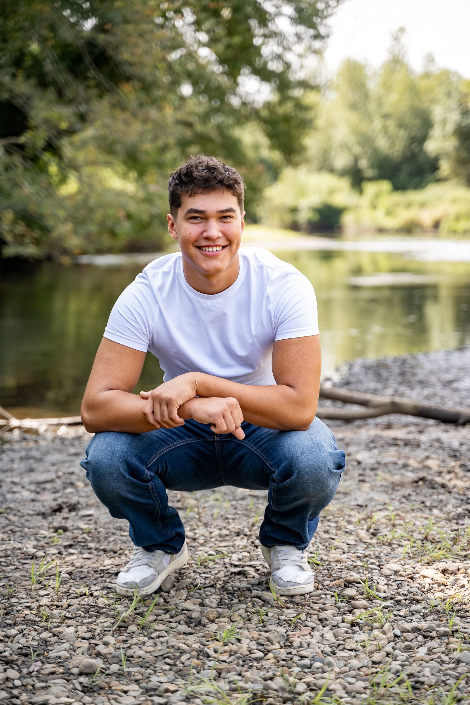 Casual outdoor senior portrait by lake with natural background and rocky shoreline in Massachusetts.