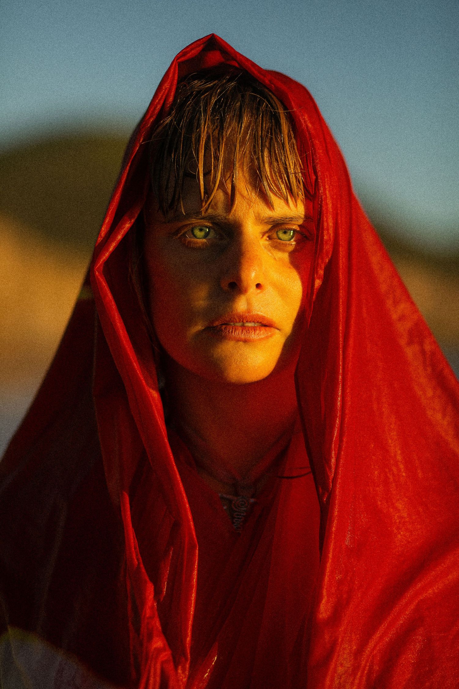 A dramatic portrait with a bright red fabric creating striking contrast against a dusky background.