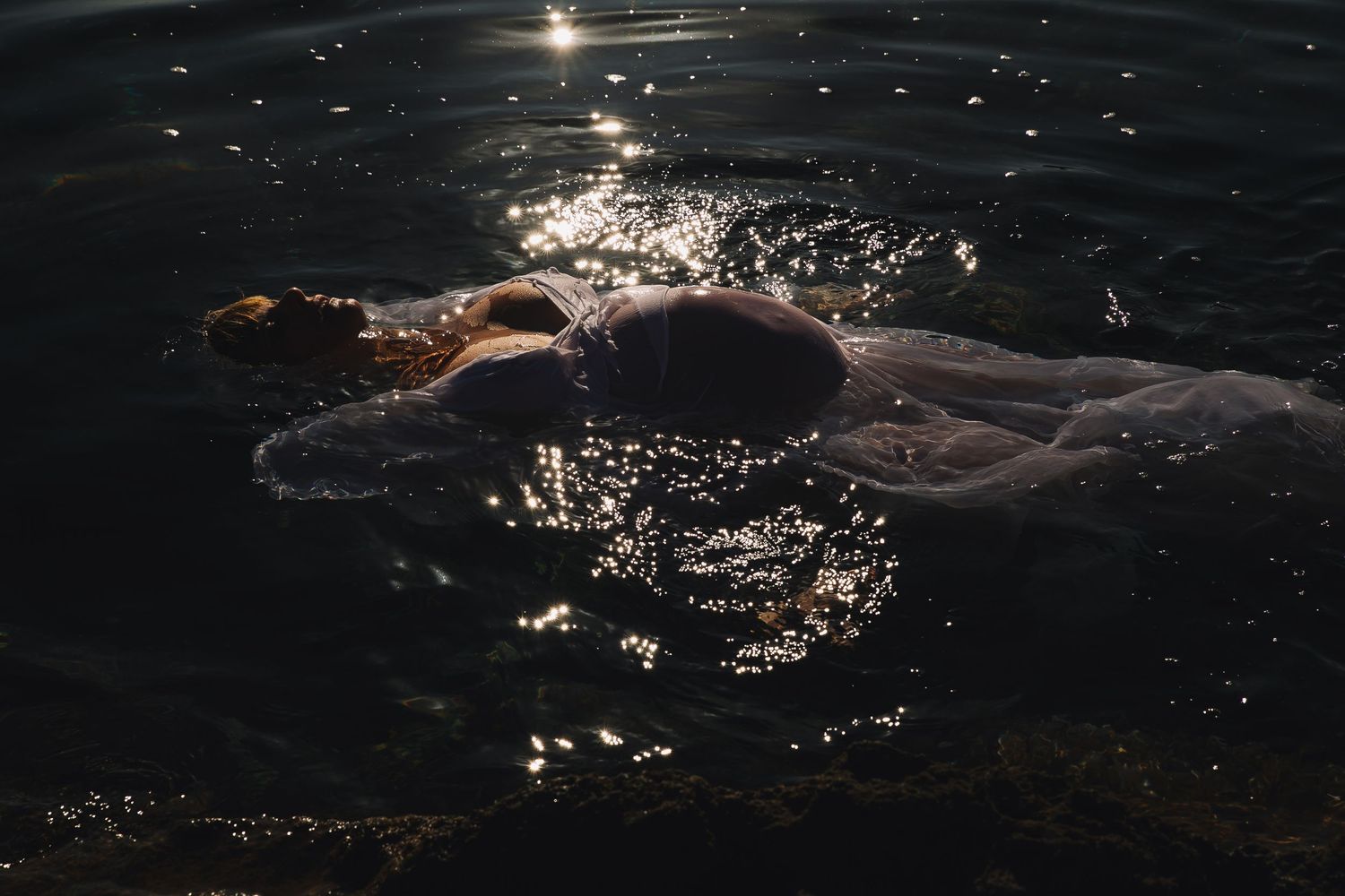 Shimmering water reflections create abstract patterns of light against a dark background.