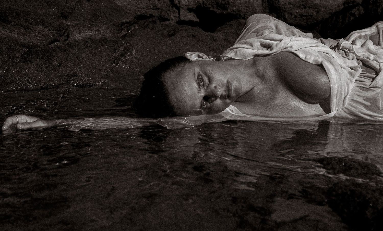 A dramatic black and white photo showing a figure lying on a dark surface.