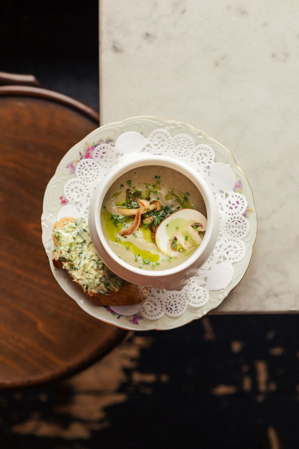 Elegant white doily plates hold creamy soup garnished with fresh herbs and microgreens on a dark wooden surface.