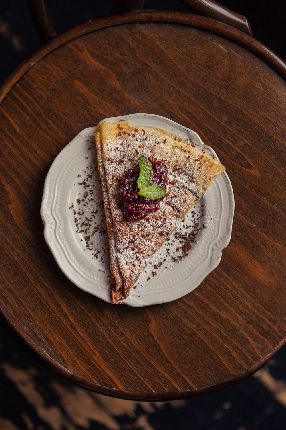 Slice of chocolate cake dusted with cocoa powder and garnished with a mint leaf on a white plate.