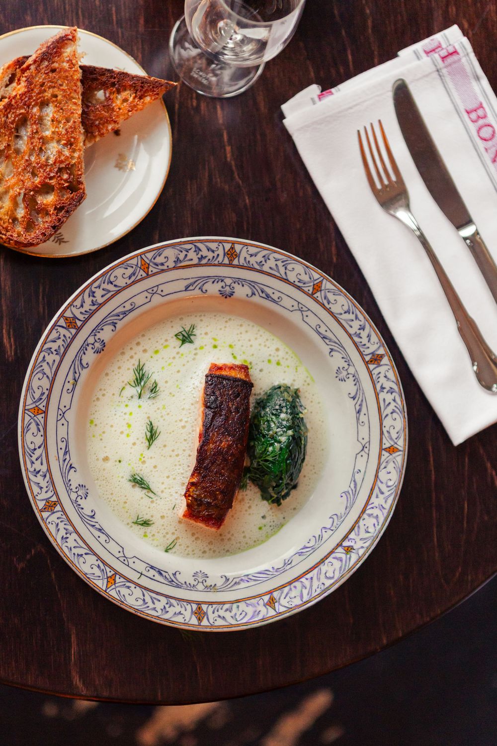 Elegant plated salmon dish with cream sauce and spinach served with crusty bread on ornate china plate.