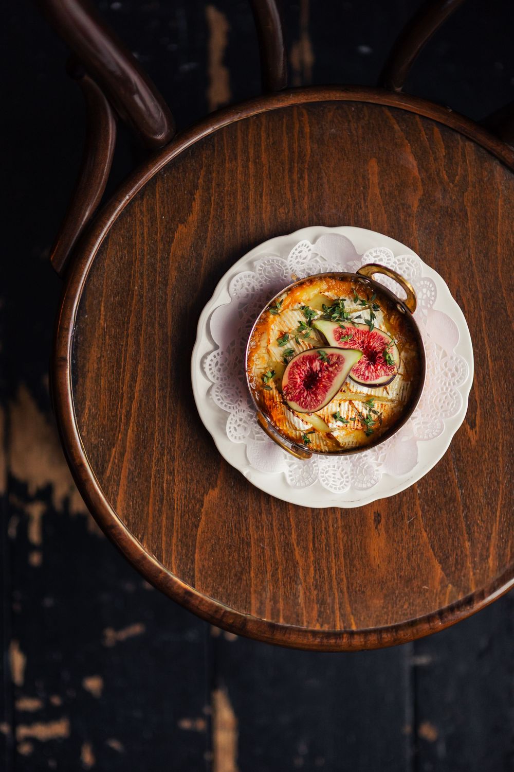 Overhead view of a white plate with baked eggs and tomatoes on a rustic wooden round table against dark background.