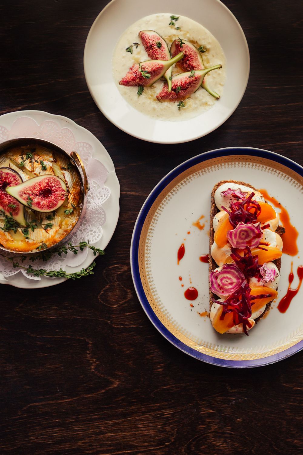 Three elegant plates featuring fig dishes including a creamy soup, roasted preparation, and toast topped with pickled onions.