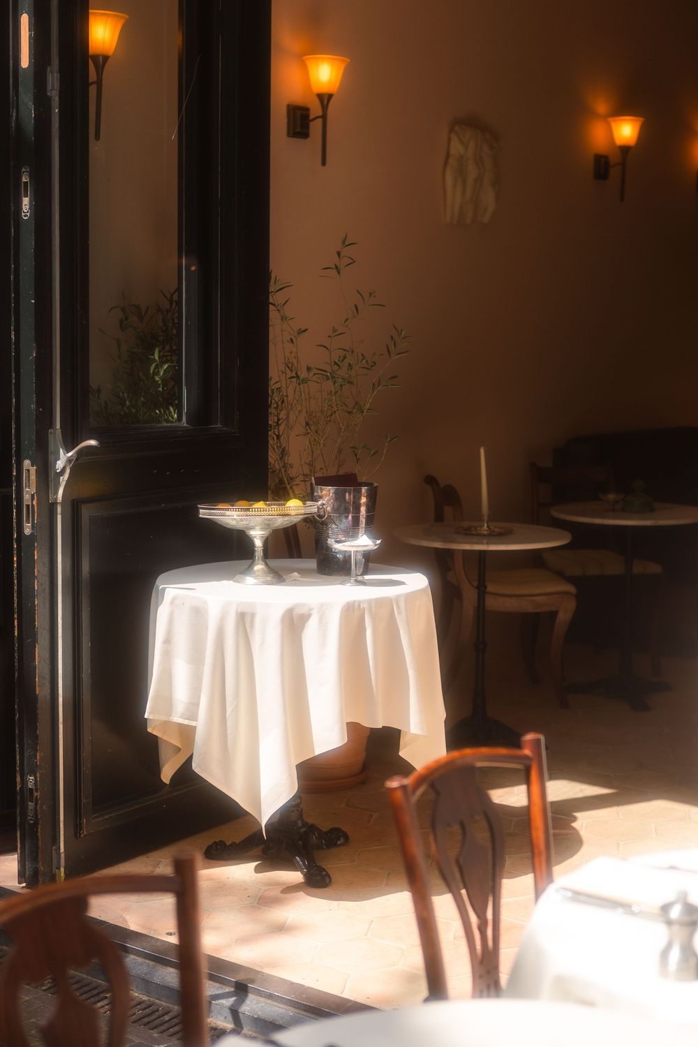 Restaurant interior with round tables covered in white tablecloths and warm lighting from wall sconces creates an elegant ambiance.