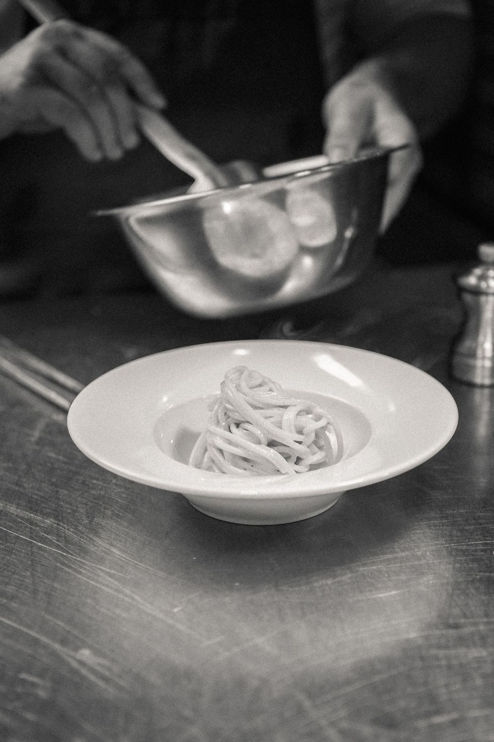 Black and white photo sequence shows pasta being served onto multiple white plates on a textured surface.