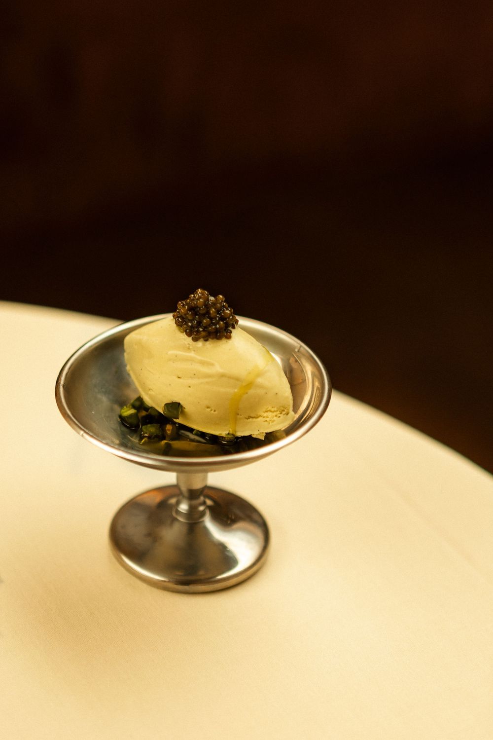 An elegant dessert presentation featuring ice cream topped with caviar in a silver coupe dish.