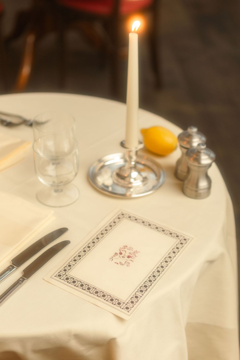 White tablecloth setting with candle and ornate napkin details in restaurant.