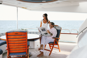 Couple enjoying leisure time reading newspapers on a luxury yacht deck with orange chairs overlooking the ocean.