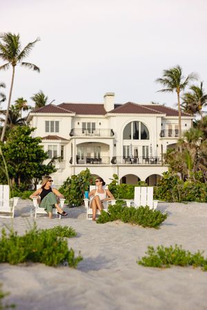 Luxurious beachfront Mediterranean-style mansion with palm trees and sandy beach access.