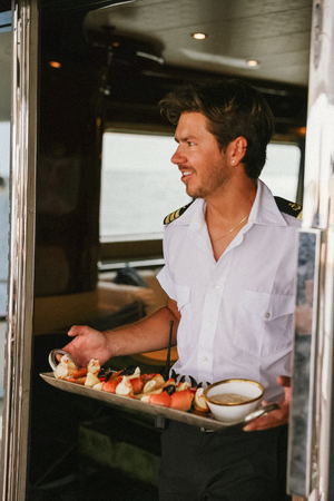 Yacht crew member serving appetizers on a silver tray in nautical uniform.