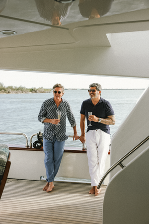 Two men enjoying drinks while standing on luxury yacht deck near ocean.