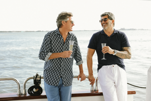 Two men sharing laughs and drinks while standing on yacht deck by water.