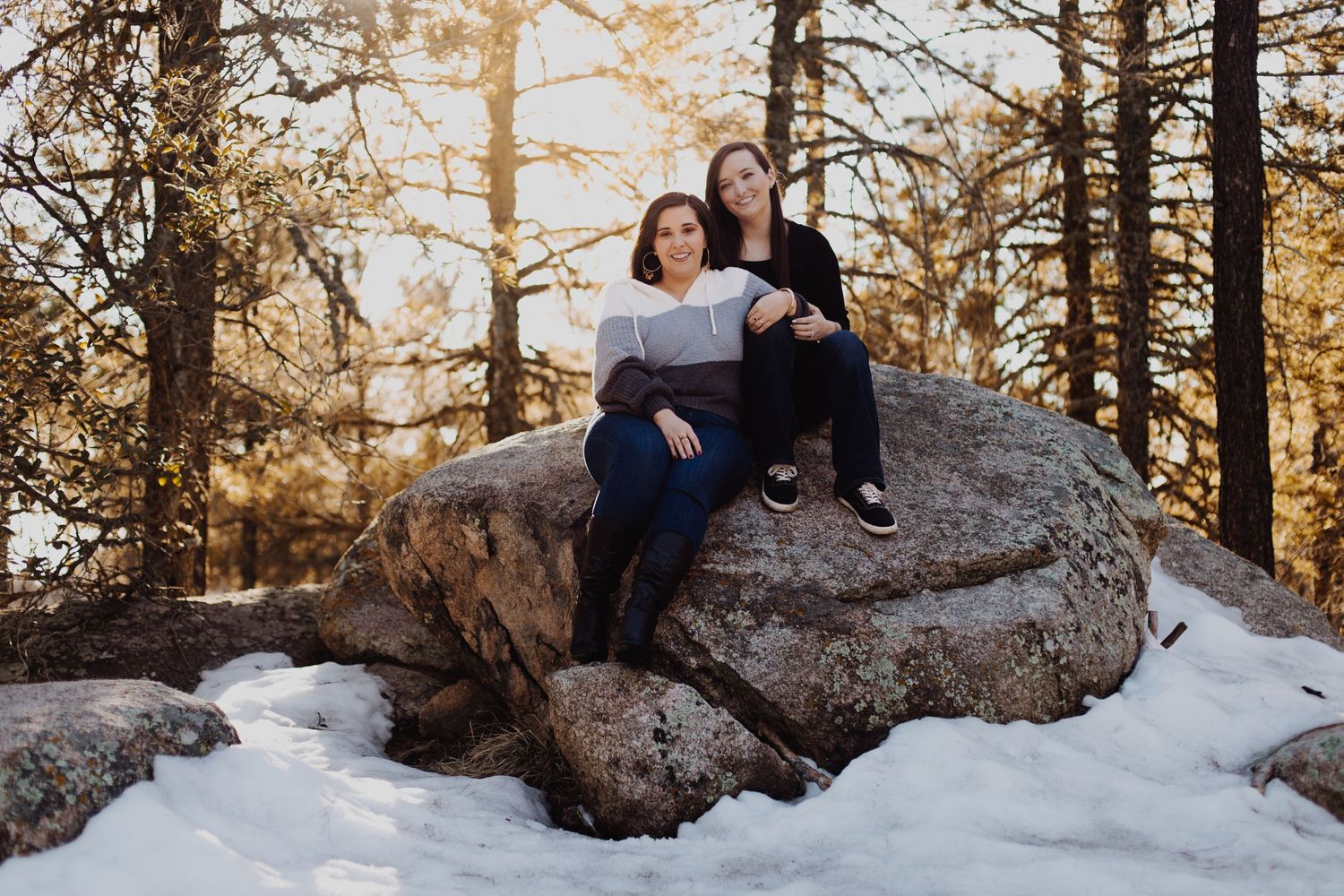 Person in white sweater and jeans sits on rock during golden hour.