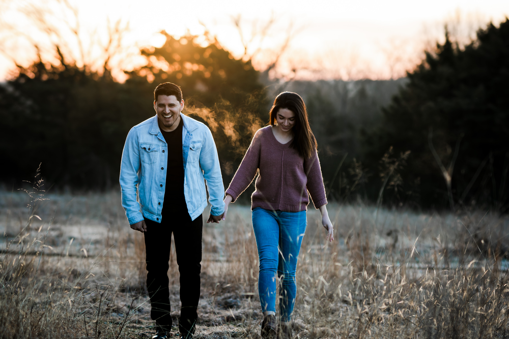 Couple walking together at sunset through a golden field while holding hands.