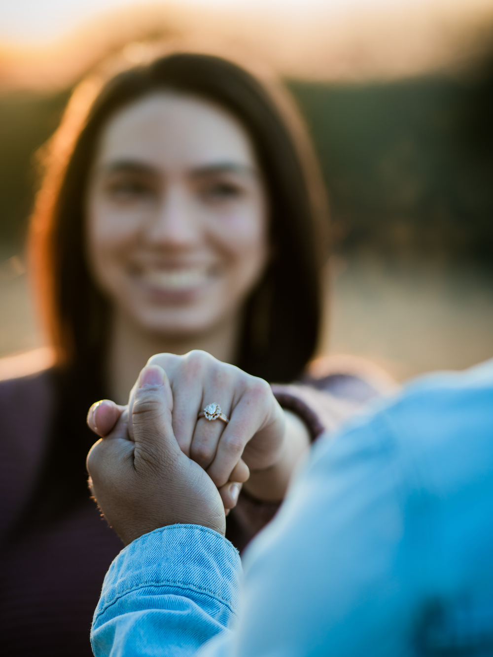 Close up shot of hands clasped together showing an engagement ring at golden hour.