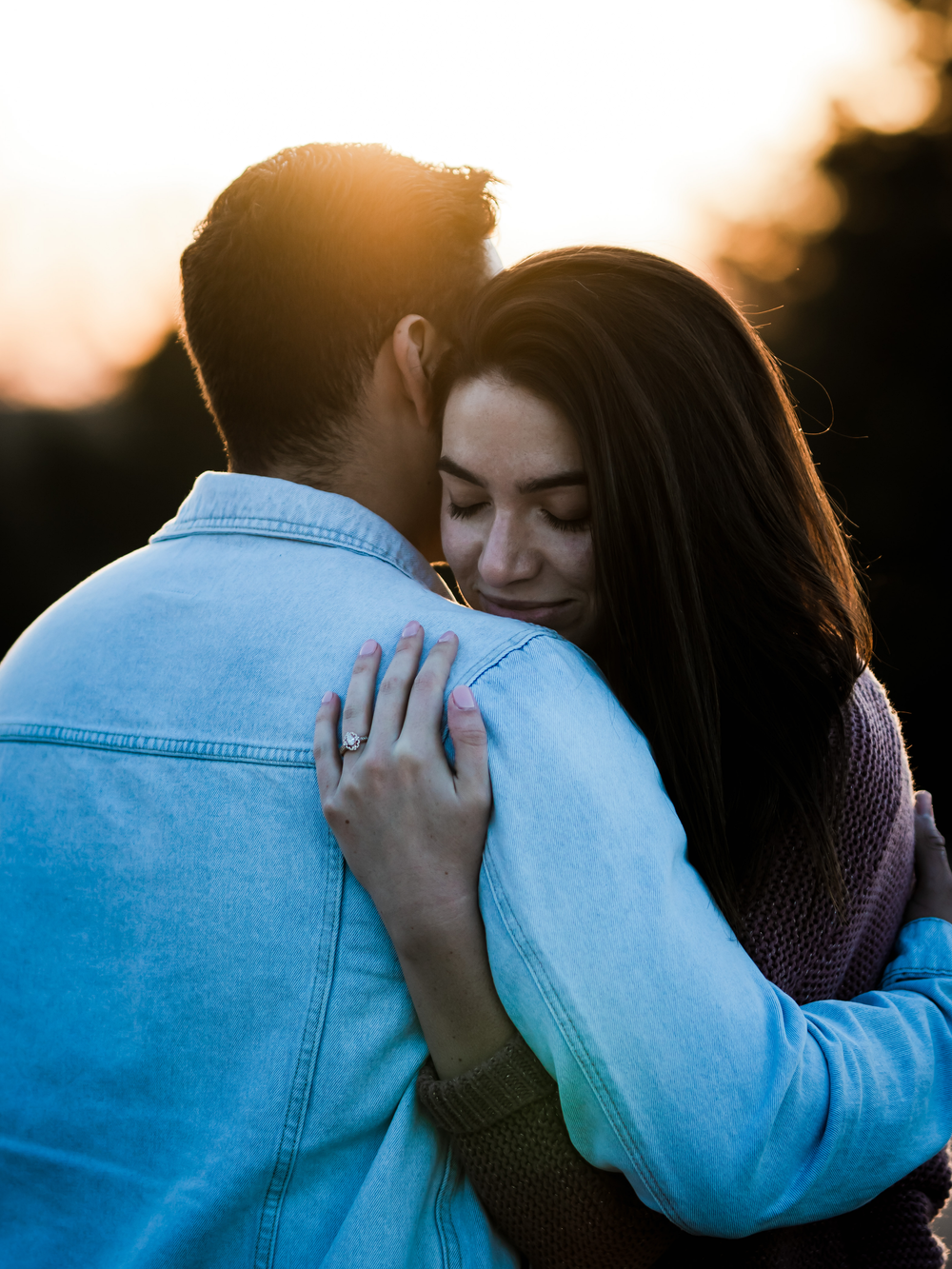 Intimate embrace between couple wearing denim jacket and sweater at sunset.