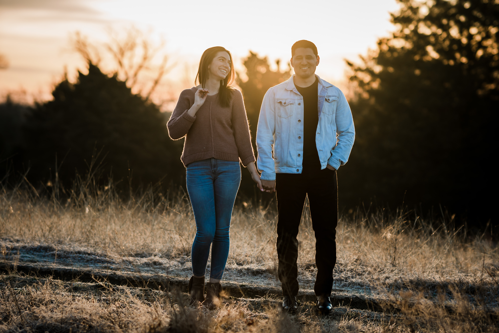 Couple walking and laughing together on a path during golden hour sunset.
