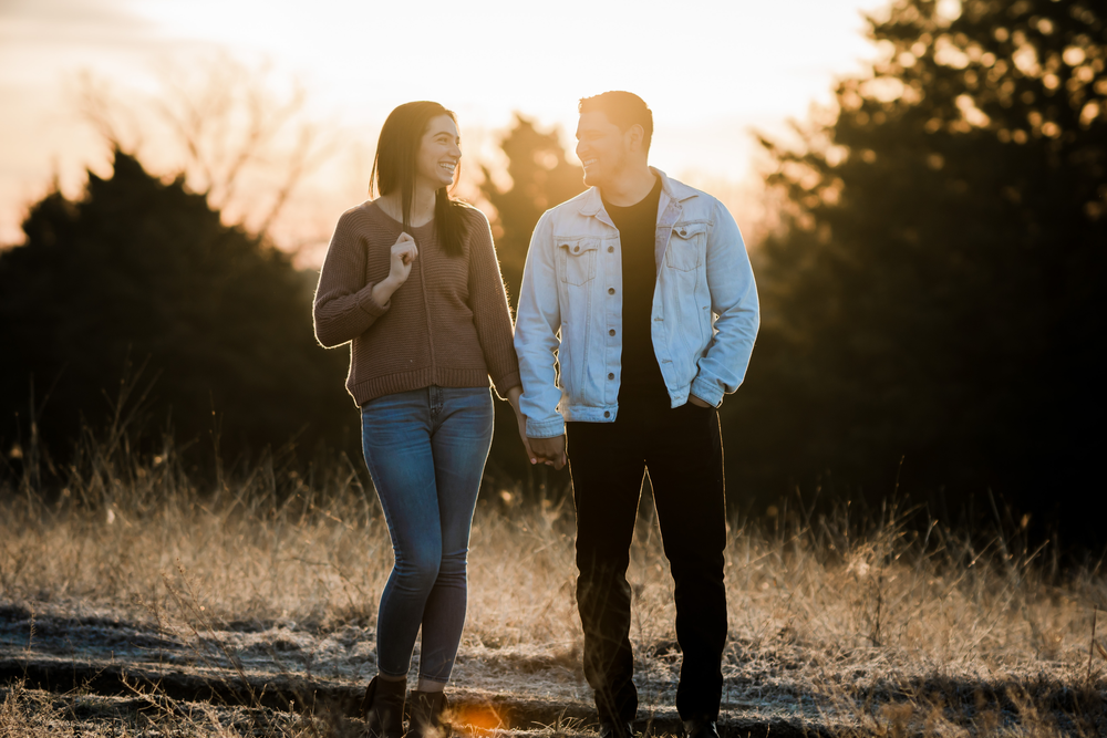 Couple sharing a romantic moment while walking through tall grass at sunset.