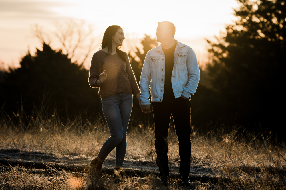 Couple strolling together through a sunlit field at dusk.