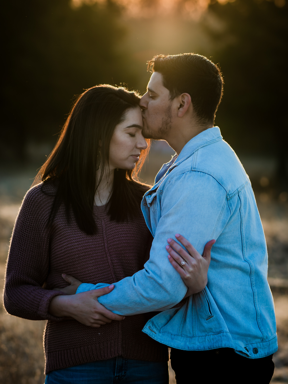 Romantic sunset embrace with couple in denim jacket and sweater in autumn field.