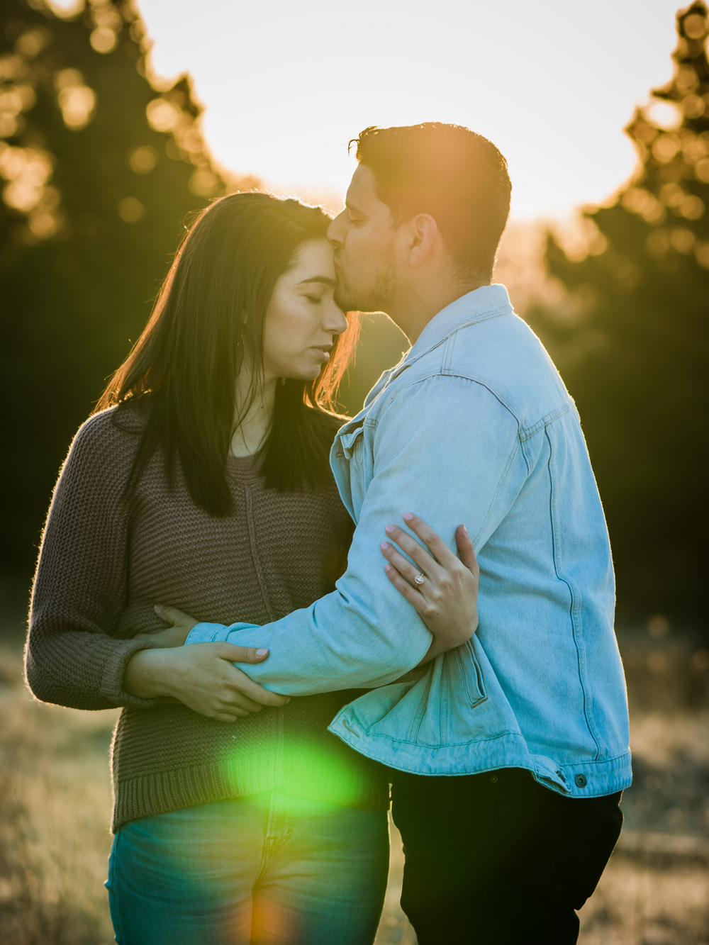 Intimate portrait of couple embracing during golden hour with sun flare.