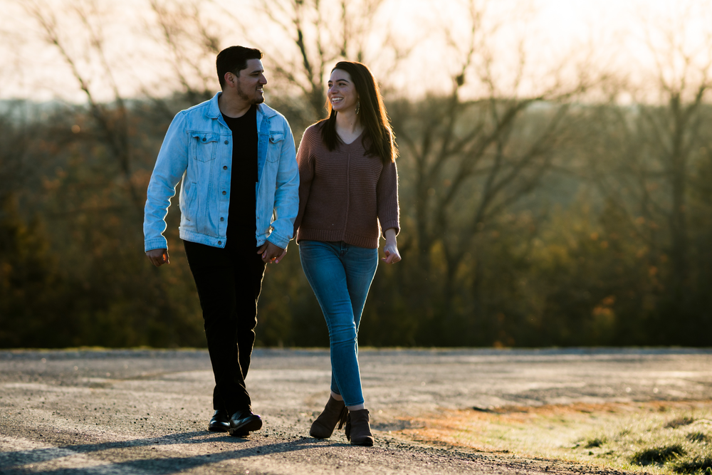 Casual couple walking together on path during sunset with autumn trees in background.
