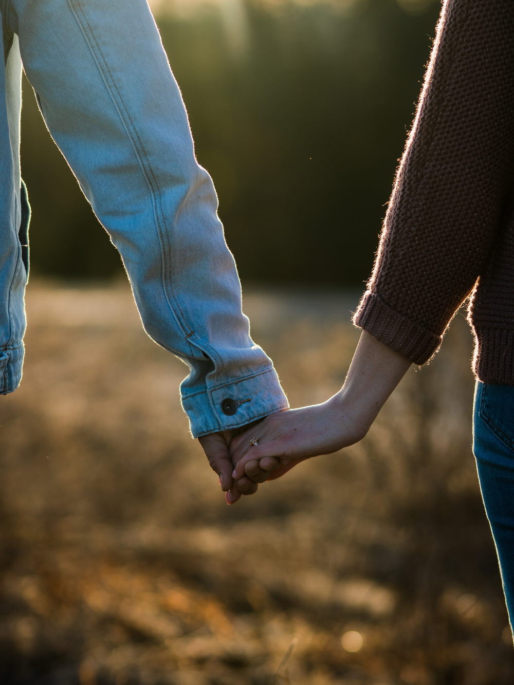 Close-up shot of couple holding hands against sunset backlight.