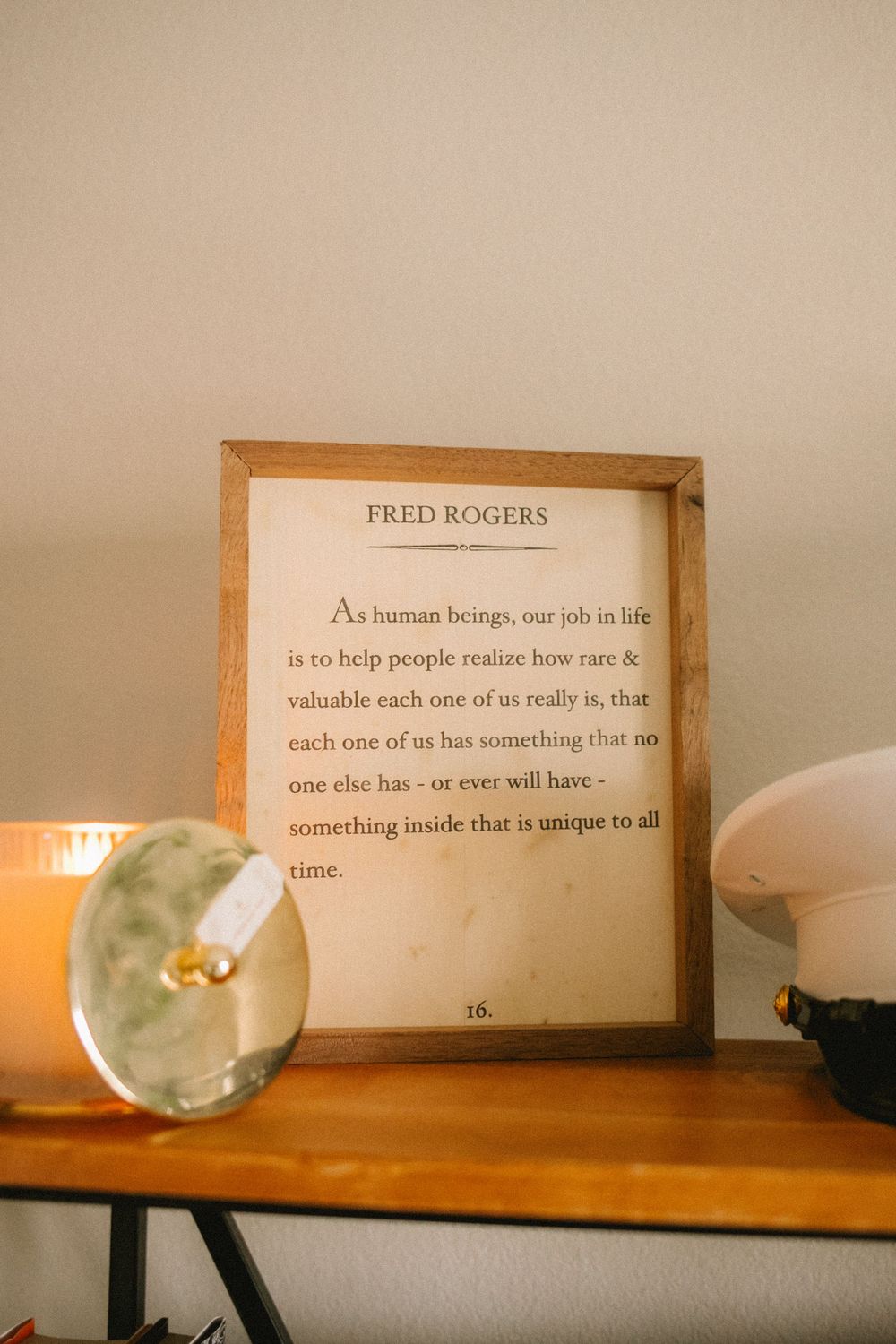 Framed Fred Rogers quote on wooden shelf beside lit candle and crystal ball home decor accent pieces.