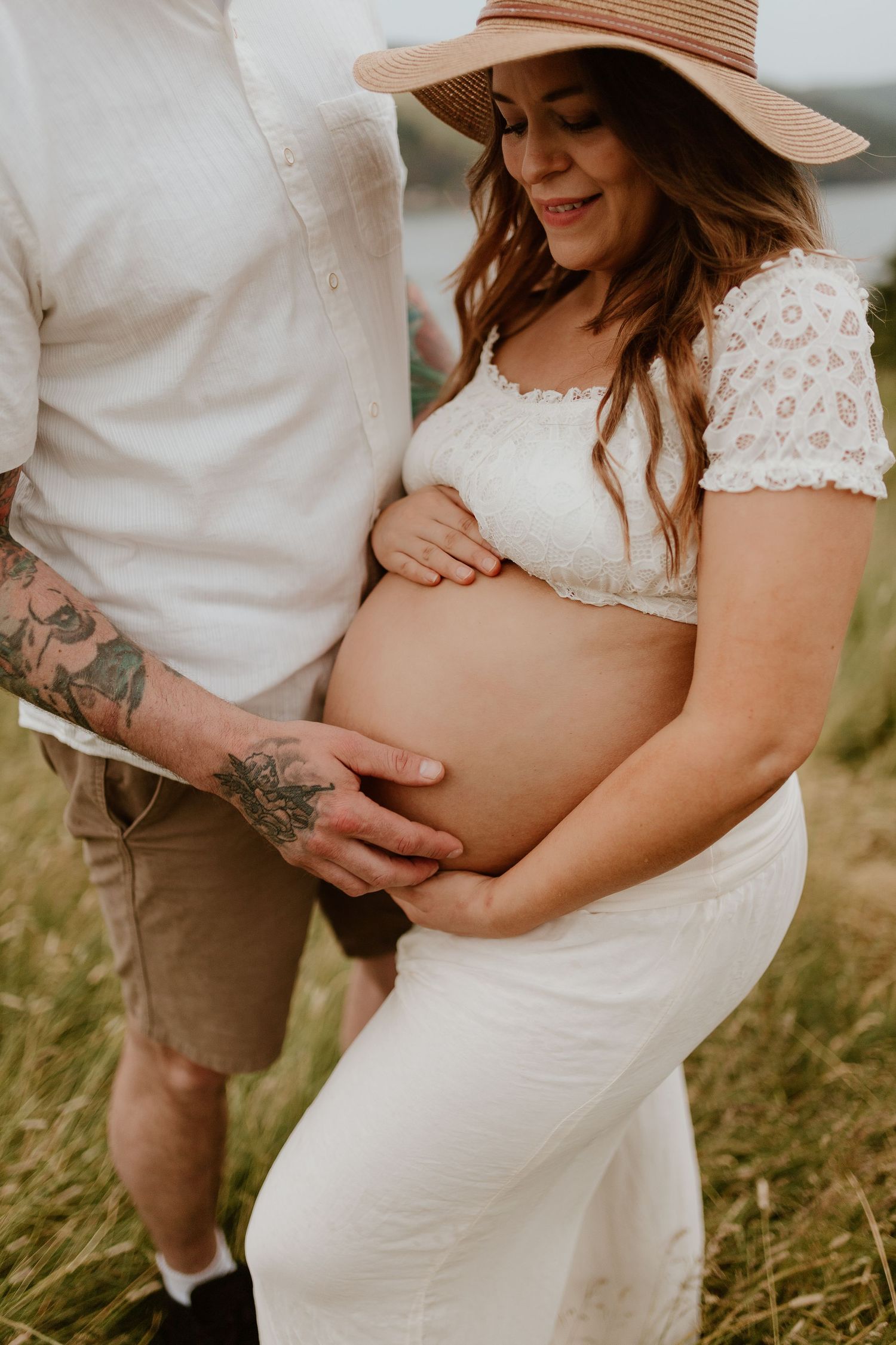 A woman looking down at her pregnant belly, and her partner rubbing her bare belly with her