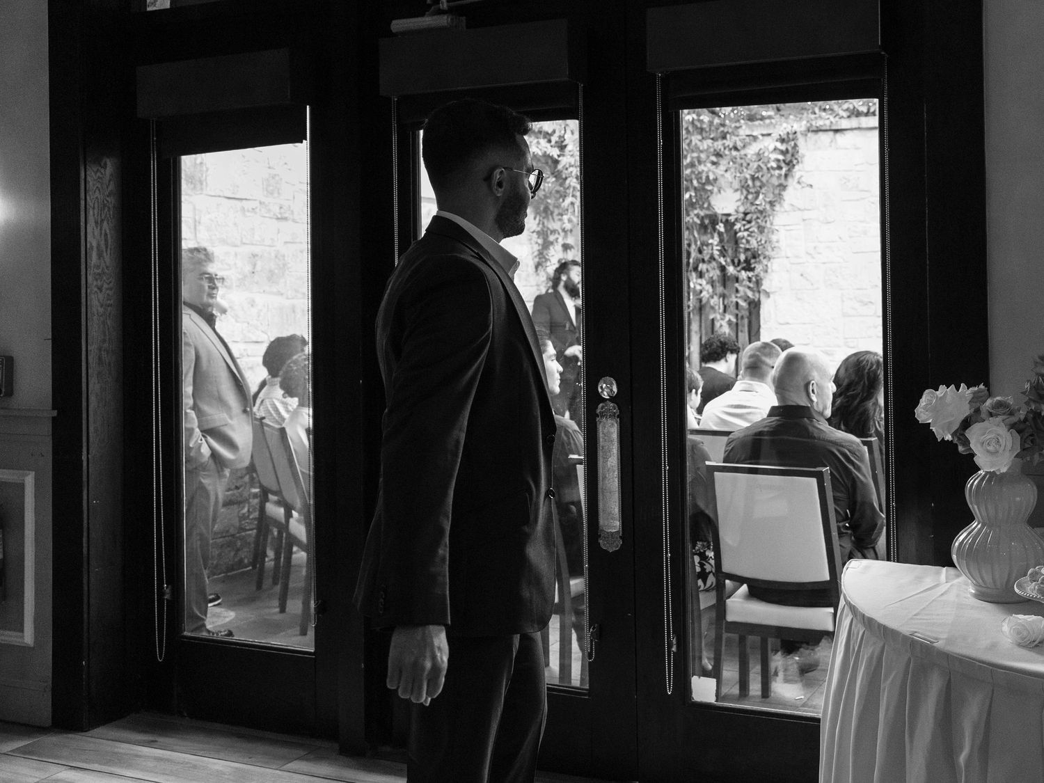 San Antonio Wedding Photography. Black and white photo of people gathered for an event through glass doors.