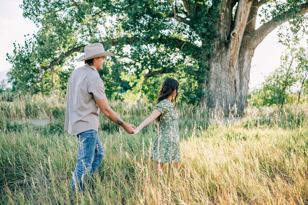 A romantic couple holding hands while walking through tall summer grass.