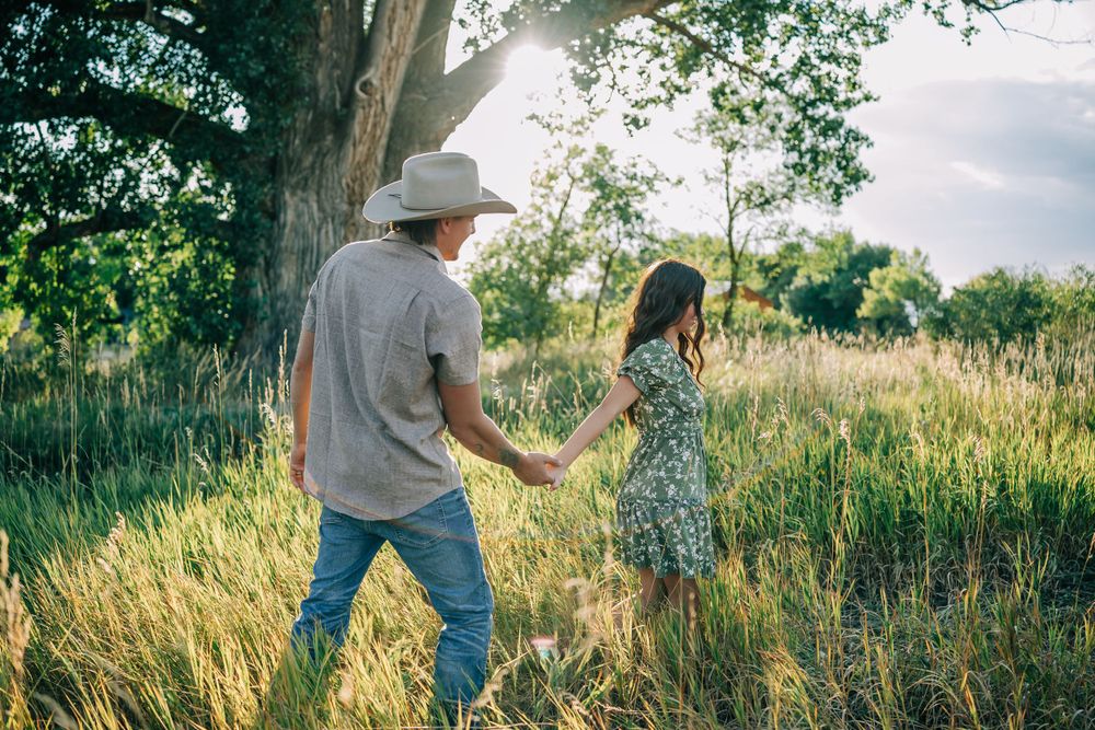 A playful couple dancing in a sun-drenched field with tall grass and trees.