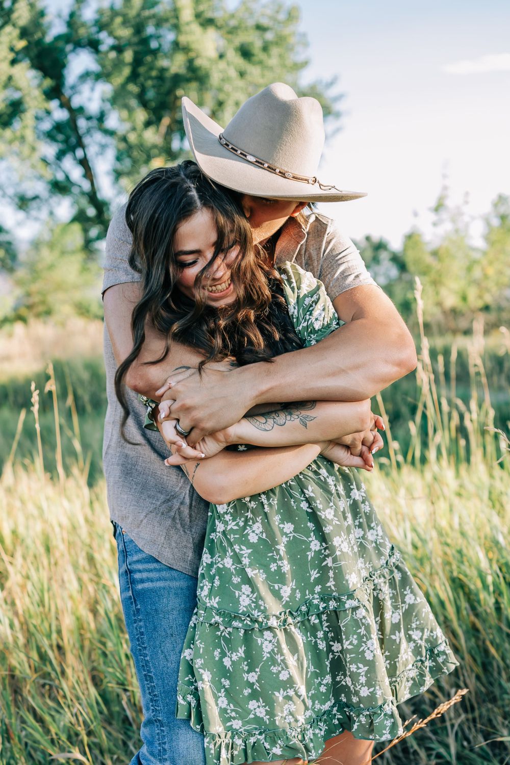 A tender embrace in a sunlit meadow with tall grass and summer foliage.