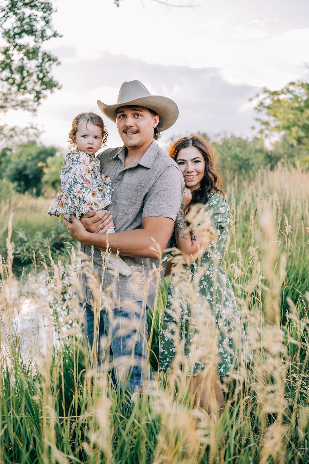 Family wearing western attire poses together in a beautiful meadow during sunset.