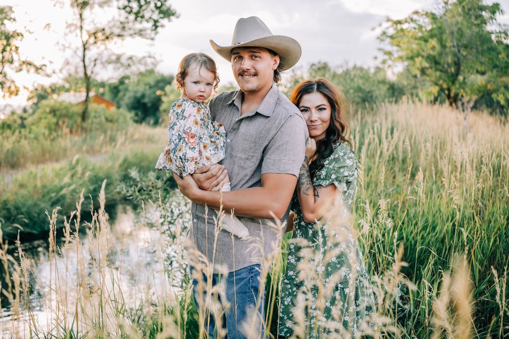 Family standing together in tall grass field during golden hour sunset.