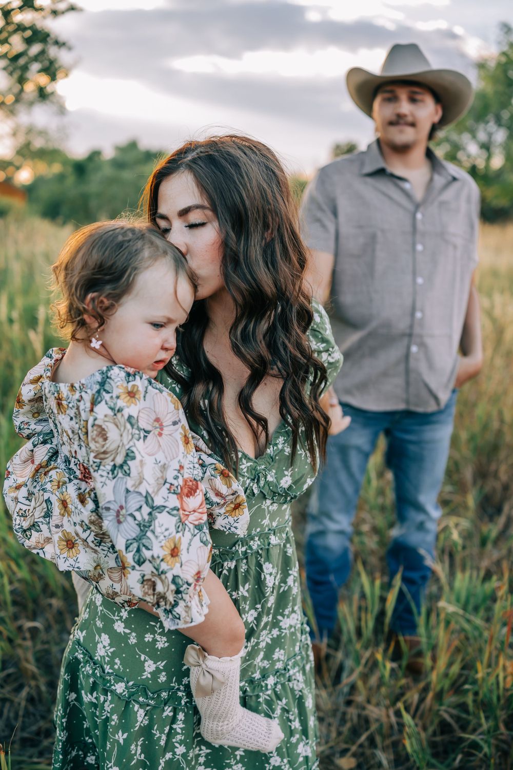 Intimate family moment captured in tall grass field during sunset.