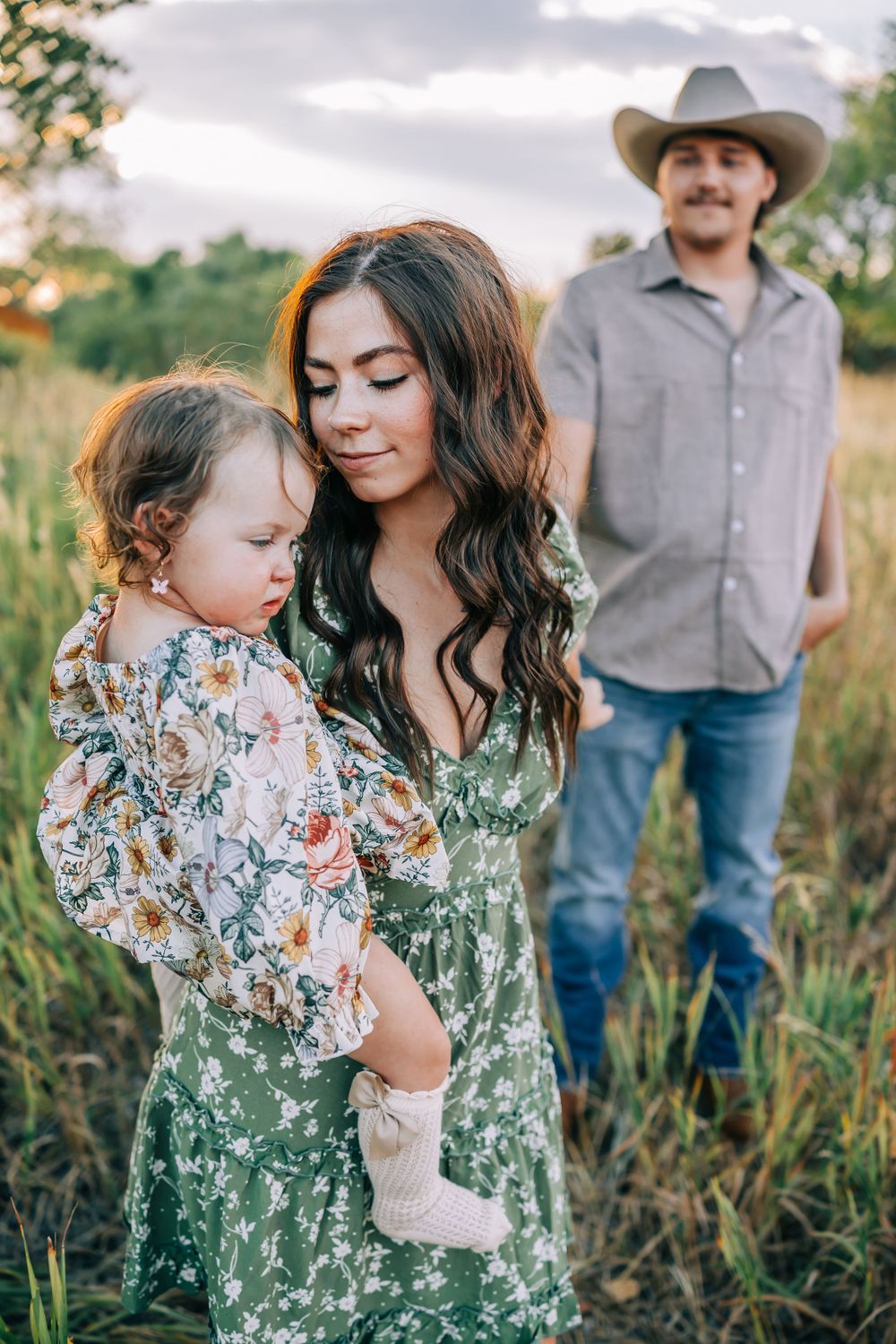 Family shares tender moment together in field during sunset.