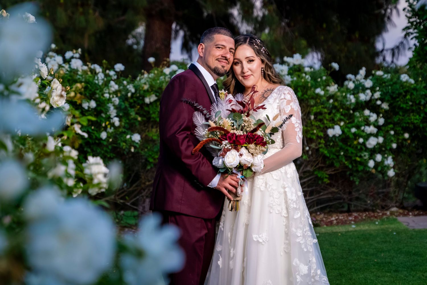 A wedding portrait featuring burgundy and cream attire amidst a garden of white flowers. granada hills.