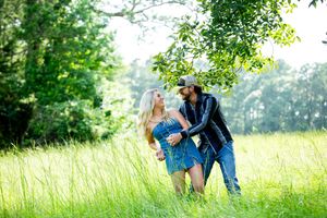 A playful couple shares a tender moment in a sunlit meadow with green trees.