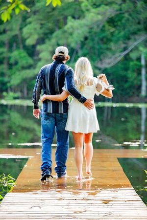 A couple stands together on a wooden dock overlooking a peaceful lake.