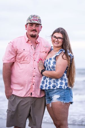 Couple in casual attire posing together on a cloudy beach.