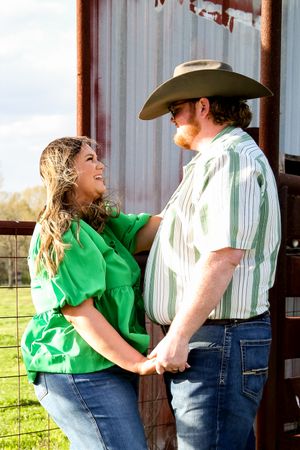 A couple shares a joyful moment together near a metal barn wall.