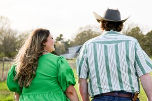 A couple in coordinating outfits stand together against a rural backdrop.